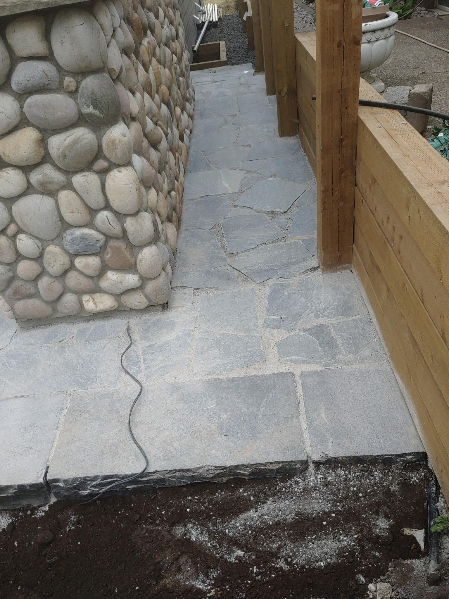 Flagstone walkway under construction with river rock wall and cedar posts